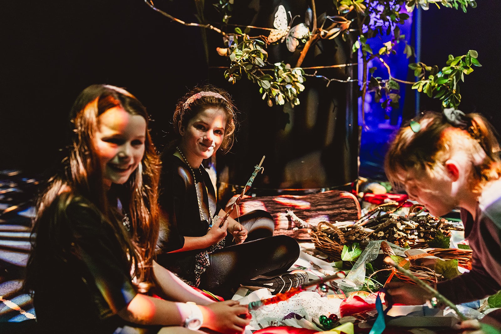 Three children sit together in dappled sunlight doing arts and crafts together during We The Young festival.